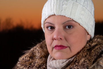 Lady outdoor extreme closeup portrait  during a beautiful cold colorful winter sunset. She is serious and looking to the camera. She is wearing season clothes.