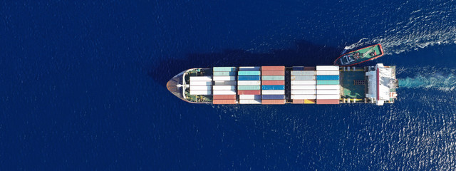 Aerial top down ultra wide photo of Container cargo Ship carrying load in truck-size colourful containers in deep blue open ocean sea 