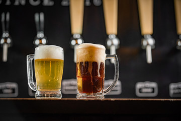 Wall Mural - Two mugs full of chopp, one with pilsen chopp and one with dark chop on a rustic table