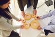 © Studio Romantic - A group of business people holds wooden wheels with teeth in their hands on an office white table.