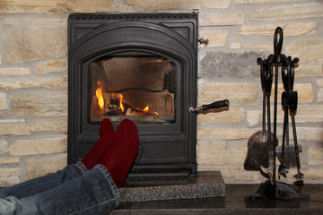 male legs in jeans and dark red socks near the hot fire of a burning fireplace, relaxation concept in winter and autumn