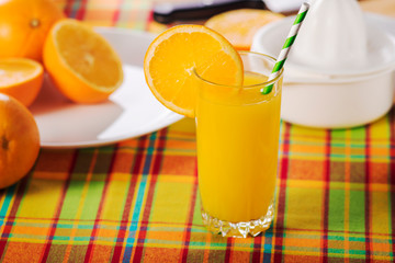 Sticker - Glass of orange juice on a table with a multi-colored tablecloth, decorated with a slice of orange.