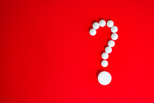 White Pills In The Form Of A Question Mark On A Red Background With Copy Space For Text.