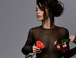 Portrait of young beautiful sexy brunette woman in black transparent clothing holding flowers on nipples places