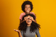 © Brastock Images - African American boy holding his mother closed eyes. Yellow background. Mothers Day. Brazilian family.