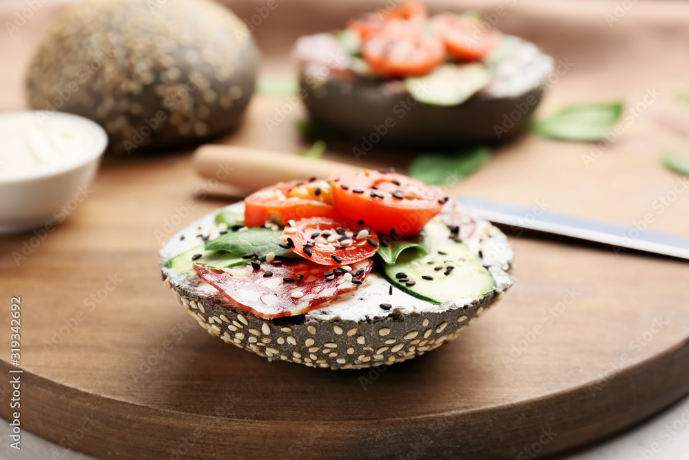 Fresh bun with tasty cream cheese, sausage and vegetables on table