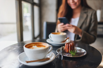 Wall Mural - Closeup image of an asian woman holding and using mobile phone with coffee cup and snack on the table in cafe