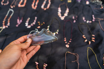 Wall Mural - Man's hand holding a big transparent stone. Farmer's market home made jewelery stand. Other necklaces on a blue cloth in the blurry background. 