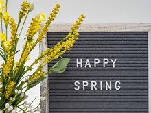 Happy Spring In White Letters On Letter Board With Yellow Flowers.
