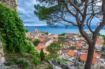 Wall Mural - Aerial panoramic view of the small town Omis surrounded with mountains, Cetina river and sea, Makarska Riviera, Croatia. View of pine tree,  old city center with red rooftops and blue see.