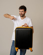 © SB Arts Media - Stylish handsome man showing suitcase. Advertising storage space for travelers and tourism image.