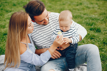 Wall Mural - A young and beautiful blonde mother in a blue dress, along with her handsome man dressed in a white jacket, siting with her little son in the summer solar park