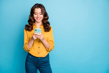 Photo of charming lady holding telephone hands reading new positive comments instagram blog post wear yellow shirt trousers isolated blue color background