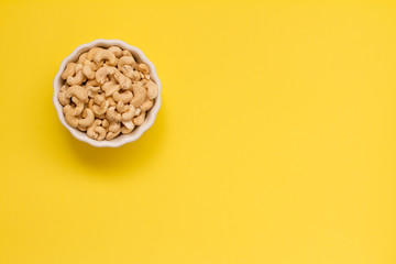 Wall Mural - cashew nuts in a white ceramic bowl on a yellow background. the concept of proper nutrition and health. Healthy food and snack, organic vegetarian food. Walnuts, pistachios, almonds, hazelnuts