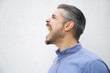 © Mangostar - Side view of angry young man screaming. Angry man screaming loud with wide open mouth. Negative emotion concept