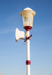 Old vintage lamppost in Blackpool England with a summer bright blue sky with soft clouds. 1860's built lighting with a modern speaker mounted on top to provide information an entertainment to public