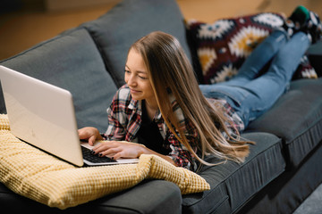 Teenage girl laying on sofa with laptop. portrait of beautiful girl at home. 