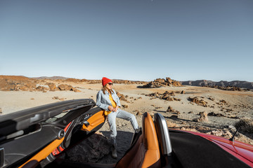 Wall Mural - Young woman traveling by convertible sports car, standing with map on the roadside of the desert valley. Wide landscape view