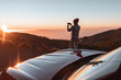 © rh2010 - Young woman photographing with phone beautiful landscape during a sunset, sitting on the car hood while traveling high in the mountains
