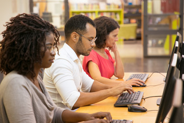 Wall Mural - Row of concentrated students using computers at library. Thoughtful young people searching information with help of computers. Education, technology concept