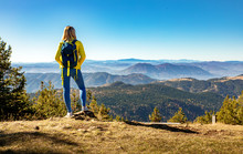 Rear View Of Female Hiker With Backpack Standing On Top Of The Mountain Enjoying The View During The Day.