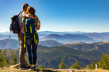Rear View Of Hikers Couple With Backpack Standing On Top Of The Mountain And Enjoying The View During The Day.