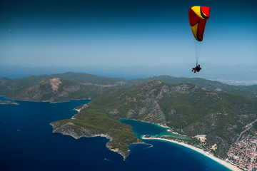 Paragliders fly in the clear blue sky in tandem over the sea and coast with beaches and lagoons