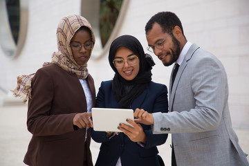 Smiling managers using tablet outdoors. African American man and Muslim women reading information from tablet. Technology concept