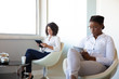 © Mangostar - Concentrated businesswomen using digital tablets. Multiethnic female colleagues sitting in chairs and using tablet computers in office during coffee break. Technology concept