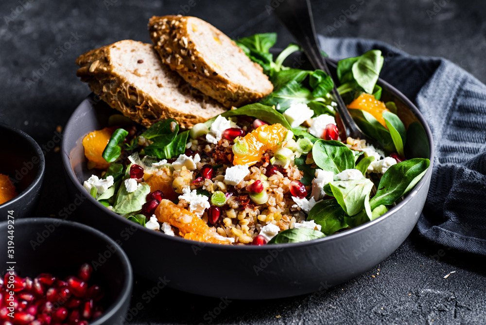 Buckwheat salad with lamb's lettuce, pomegranat seeds, goat cheese, mandarine and spring onion, Served with whole grain baguette and red wine. Black table and black background. - obrazy, fototapety, plakaty 