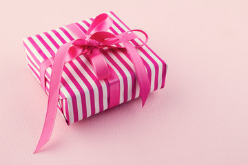 Pink and white striped gift box with a pink ribbon on a light background. Gift for mothers day woman, wedding, valentine concept. Copy space.