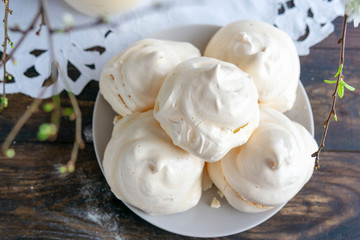 Homemade meringue cookies on plate, rustic wooden table with handmade napkin near window, flat lay with spring tree brunch. Italian, French sweet dessert made of eggs and sugar, natural light.