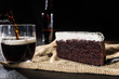 Portion of chocolate cake and black beer on black background with bottle and serving black beer in glass