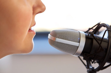 Wall Mural - technology, mass media and people concept - close up of woman with microphone talking and recording podcast at studio