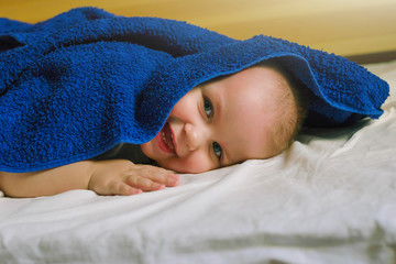 Wall Mural - Funny boy kid with a color classic blue towel on his head. Baby after bathing on the bed.