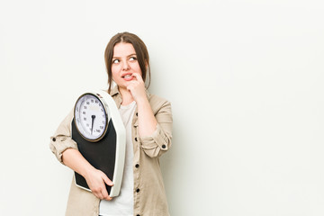 Wall Mural - Young curvy woman holding a scale relaxed thinking about something looking at a copy space.