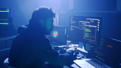 Profile of confident programmer coding technology typing on laptop in the smoky room at night.