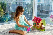 Adorable Little Girl Playing With A Dollhouse While Sitting On The Floor