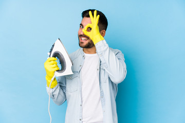 Wall Mural - Portrait of young man ironing isolated excited keeping ok gesture on eye.