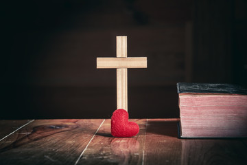 Wall Mural - Standing Cross with red heart and the holy Bible on wooden table, Close up, christian worship concept.