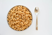 Bowl Of Whole Grain Oat Cereal With A Silver Spoon On A White Background , Back View. Heart Shapes Cereal. 