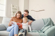 © Pixel-Shot - Happy young family reading fashion magazine while sitting on sofa at home