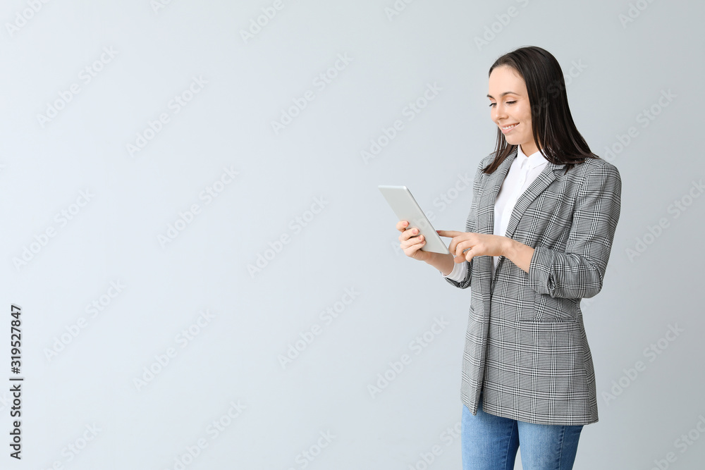 Young businesswoman with tablet computer on grey background
