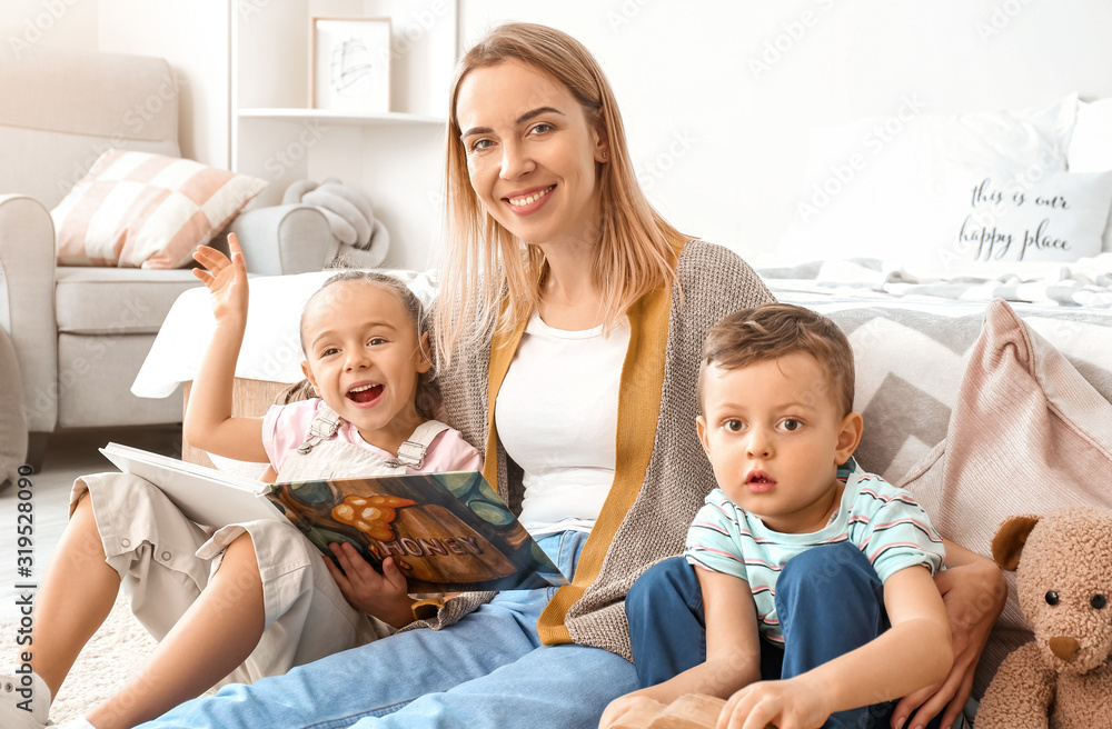 Nanny and cute little children reading book at home
