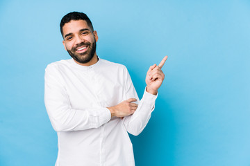 Wall Mural - Young latin man against a blue  background isolated smiling cheerfully pointing with forefinger away.