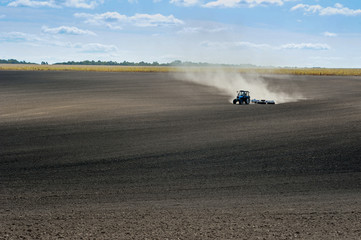 Fototapete - blue tractor on the plowed field performs the preparation for sowing.