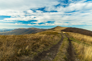 Poster - highland mountain ridge dirt trail route scenic landscape view horizon background cloudy blue sky