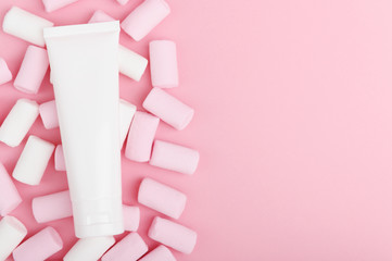 Wall Mural - Cosmetic product in white packaging on a pastel background with colorful sweets. Skincare, hand cream on a light backdrop with marshmallows. Toothpaste, lotion, moisturizer top view, copy space