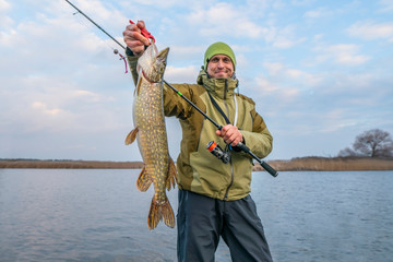 pike fishing. happy fisherman holding big fish and tackle