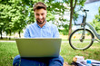© baranq - Portrait of cheerful young man having lunch break in the park using his laptop